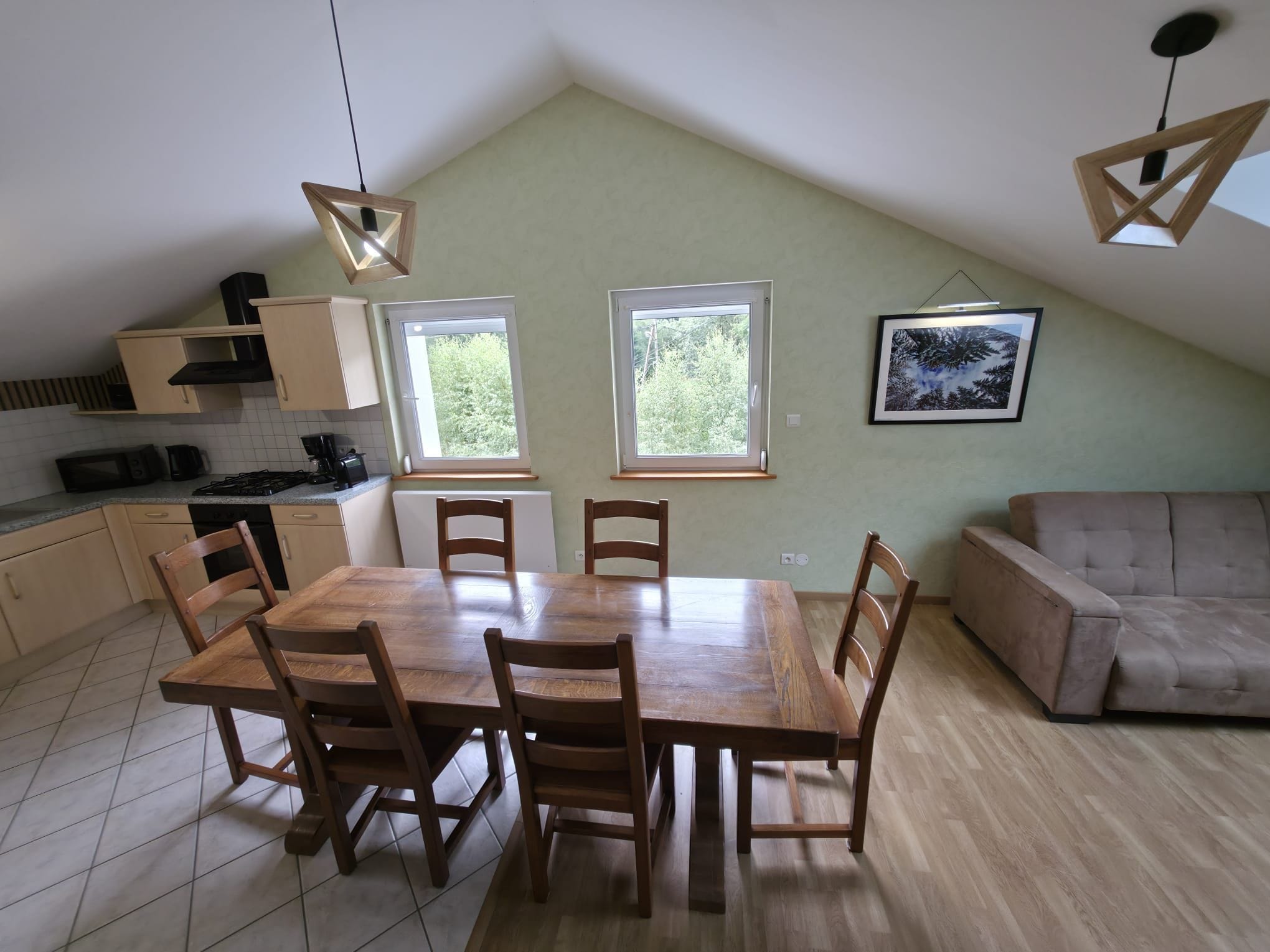 Un comedor con mesa y sillas de madera, una cocina con armarios y electrodomésticos, y un ventanal con vista a árboles.