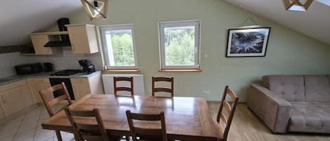 Un comedor con mesa y sillas de madera, una cocina con armarios y electrodomésticos, y un ventanal con vista a árboles.