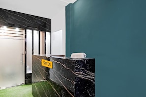A reception area with a marble counter, a sign reading 'SPOT ON', and a green wall. - Hotel O AK Residency (Noida)