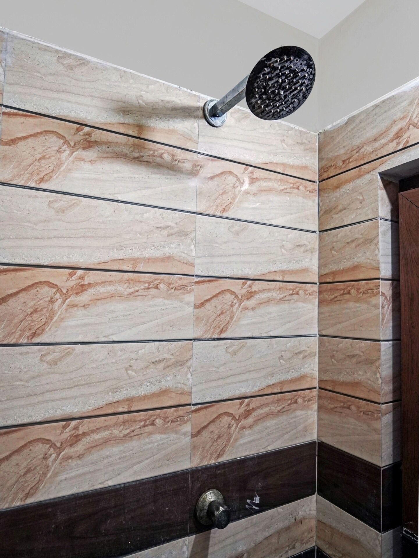 Une salle de bain avec un mur recouvert de carreaux présentant un motif évoquant le marbre et une pomme de douche fixée au mur.