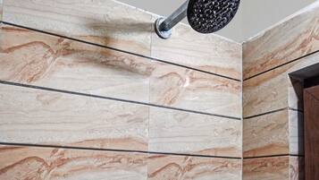 Une salle de bain avec un mur recouvert de carreaux présentant un motif évoquant le marbre et une pomme de douche fixée au mur.