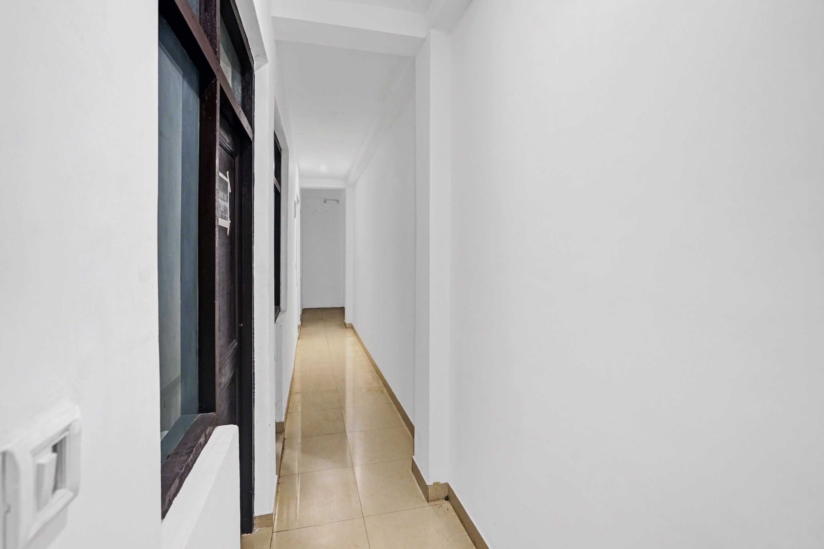 A narrow hallway with white walls and a tiled floor, leading to a door at the end.