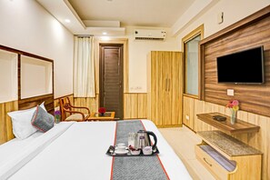 Een hotelkamer met een bed, een aan de muur bevestigde televisie, een houten garderobe en een klein tafeltje met ontbijtartikelen.