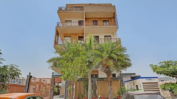 Un immeuble résidentiel à plusieurs étages, doté de balcons, d’une entrée sécurisée et d’un palmier au premier plan.