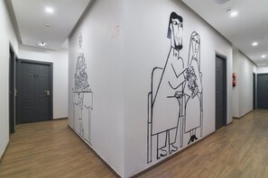 Un passadís amb un mural gran a la paret, portes i un extintor.