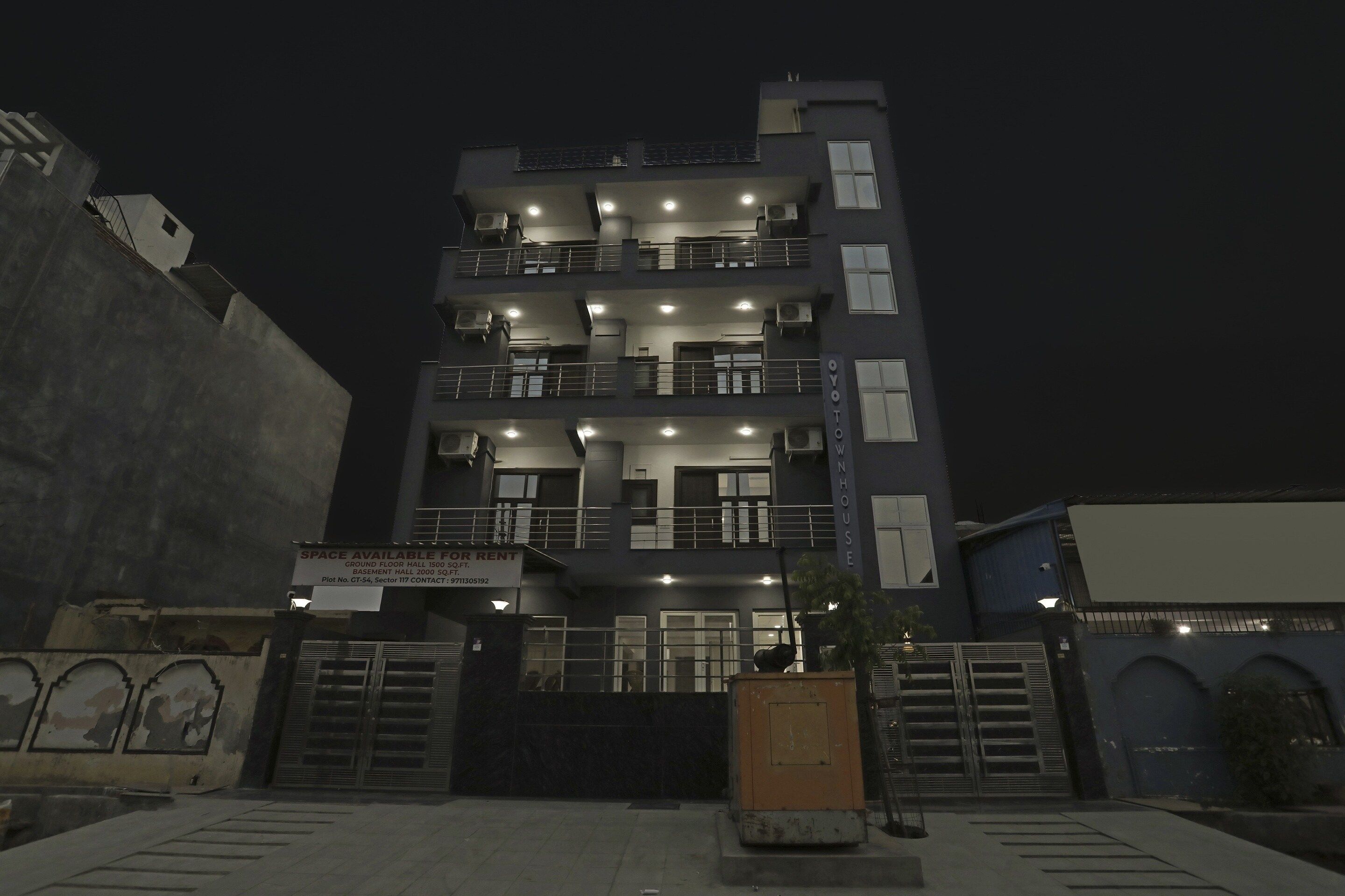 Een meerhoog gebouw met balkons, een hek en een bord waarop staat dat er huurruimte beschikbaar is.