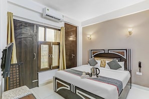 Une chambre d’hôtel équipée d’un lit, d’une table de chevet, de rideaux, d’un climatiseur et d’un luminaire fixé au mur.