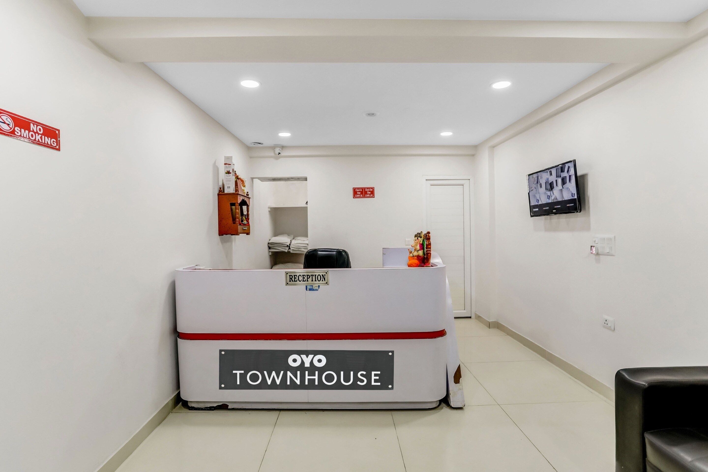 Un espace d’accueil avec un comptoir de réception portant l’inscription « OYO TOWNHOUSE », un panneau « DÉFENSE DE FUMER », une caméra de surveillance et un téléviseur fixé au mur.