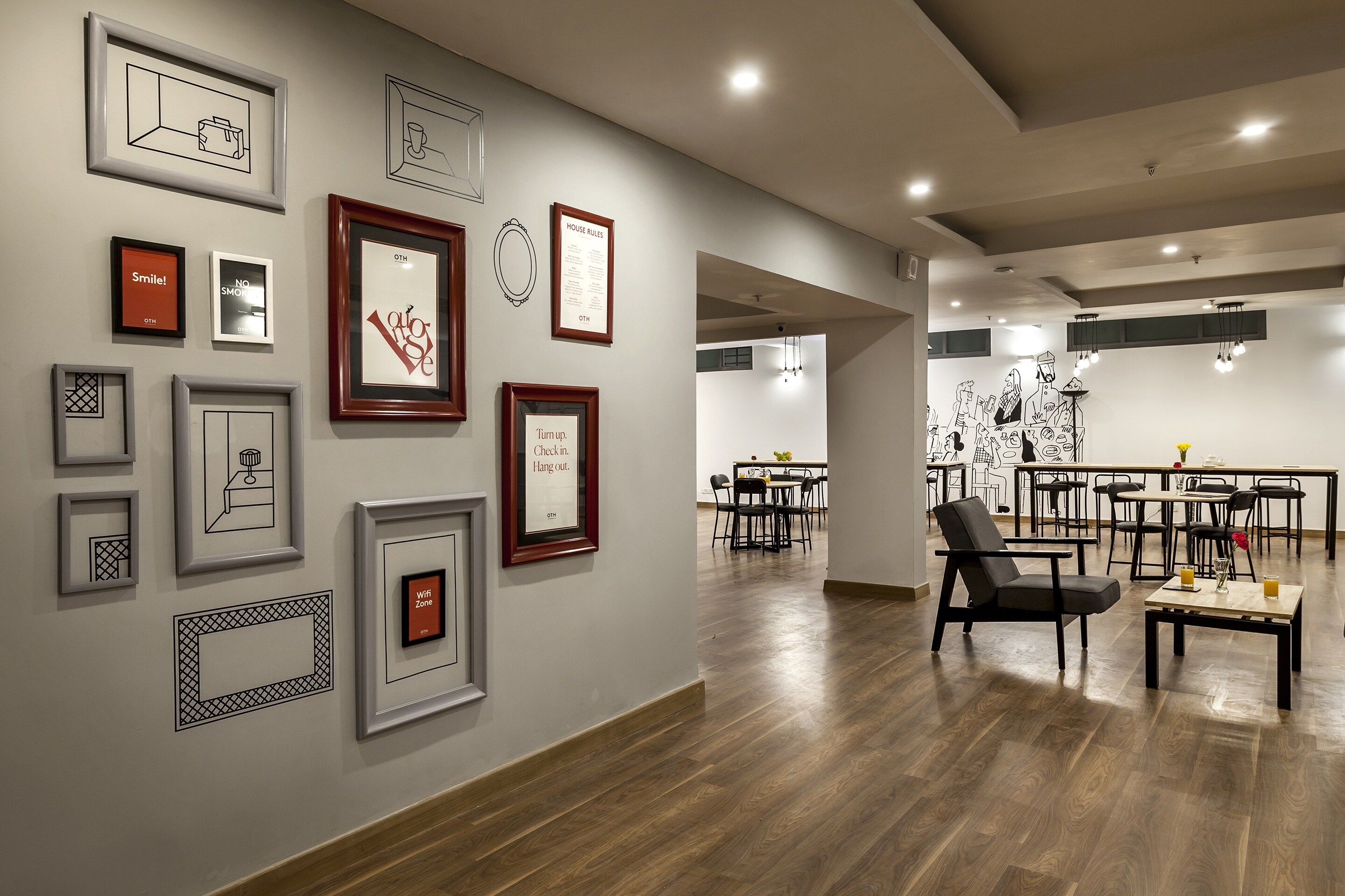 Un intérieur moderne avec des œuvres d’art encadrées accrochées aux murs, un coin repas avec des tables et des chaises, et un plancher en bois.