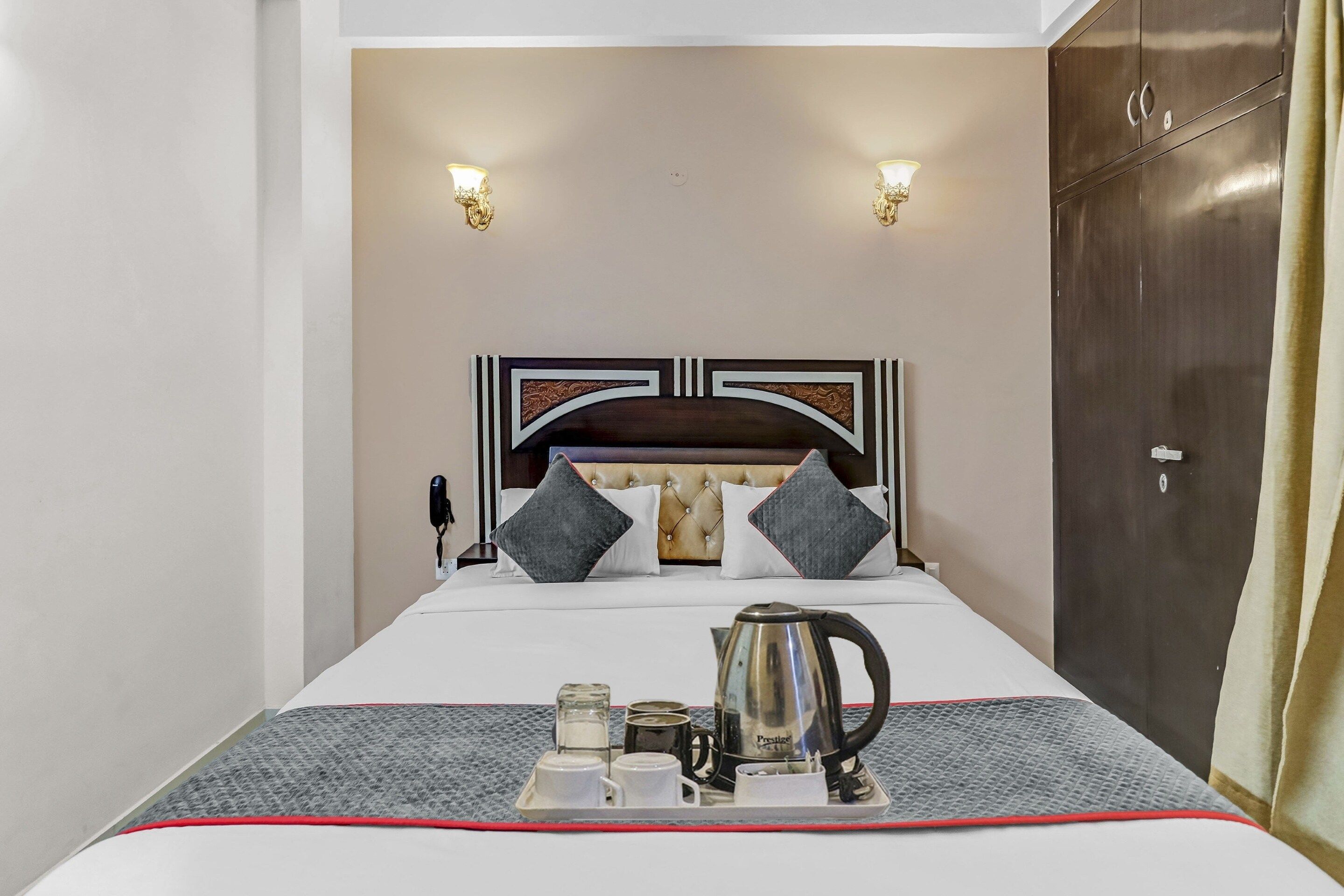 Una habitación de hotel con una cama, una mesita de noche con una tetera, tazas y una bandeja, además de un armario.