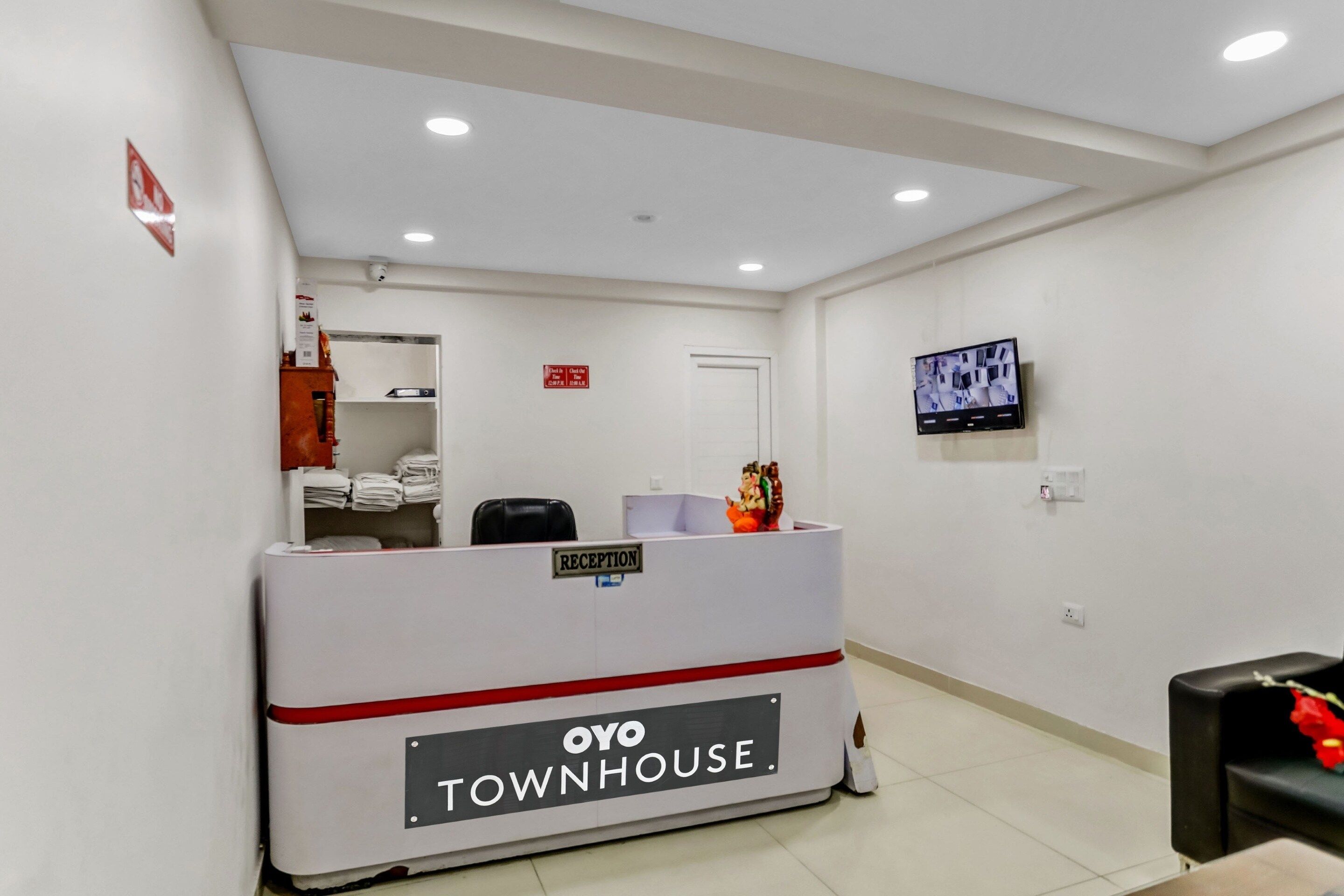 Un espace d’accueil avec un comptoir de réception portant l’inscription « OYO TOWNHOUSE », un téléviseur fixé au mur et une porte visible au fond.