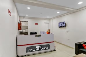 Un espace d’accueil avec un comptoir de réception portant l’inscription « OYO TOWNHOUSE », un téléviseur fixé au mur et une porte visible au fond.