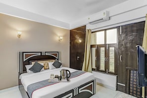 Une chambre d’hôtel équipée d’un lit, d’une table de chevet, d’une lampe fixée au mur, d’un appareil de climatisation et d’une fenêtre avec des rideaux.