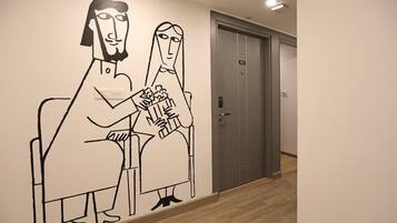A wall with a simple line drawing of two people sitting, a door with a number, and a light fixture.
