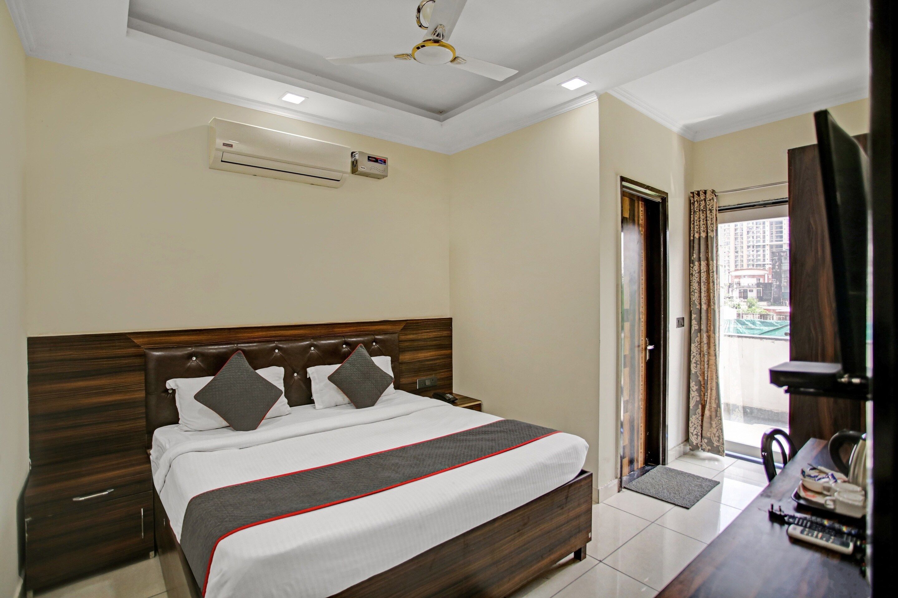 Habitación de hotel con cama, mesita de noche y vistas a la ciudad por la ventana.
