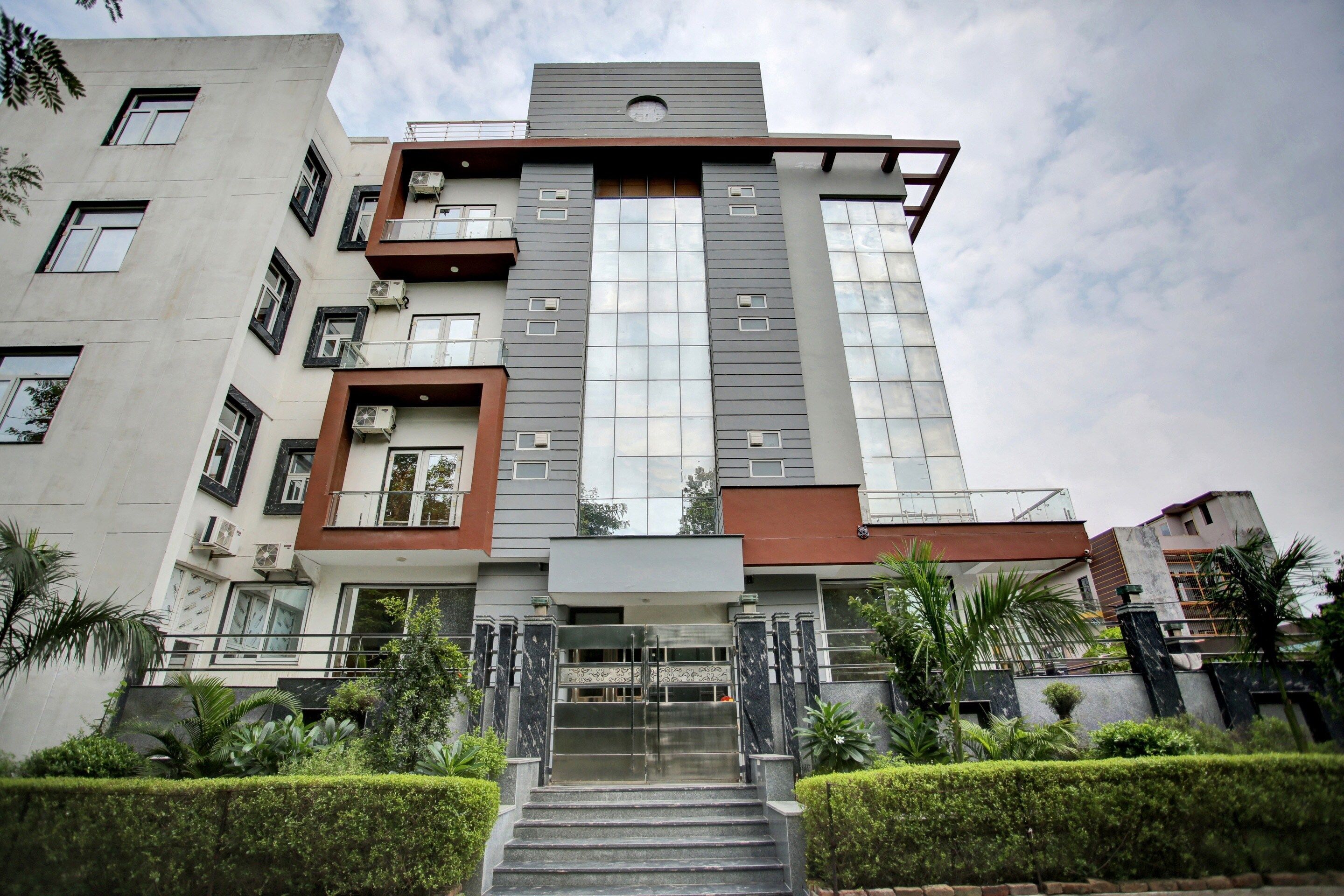 Un edificio de varios pisos con una entrada central, rodeado de setos cuidados y palmeras.