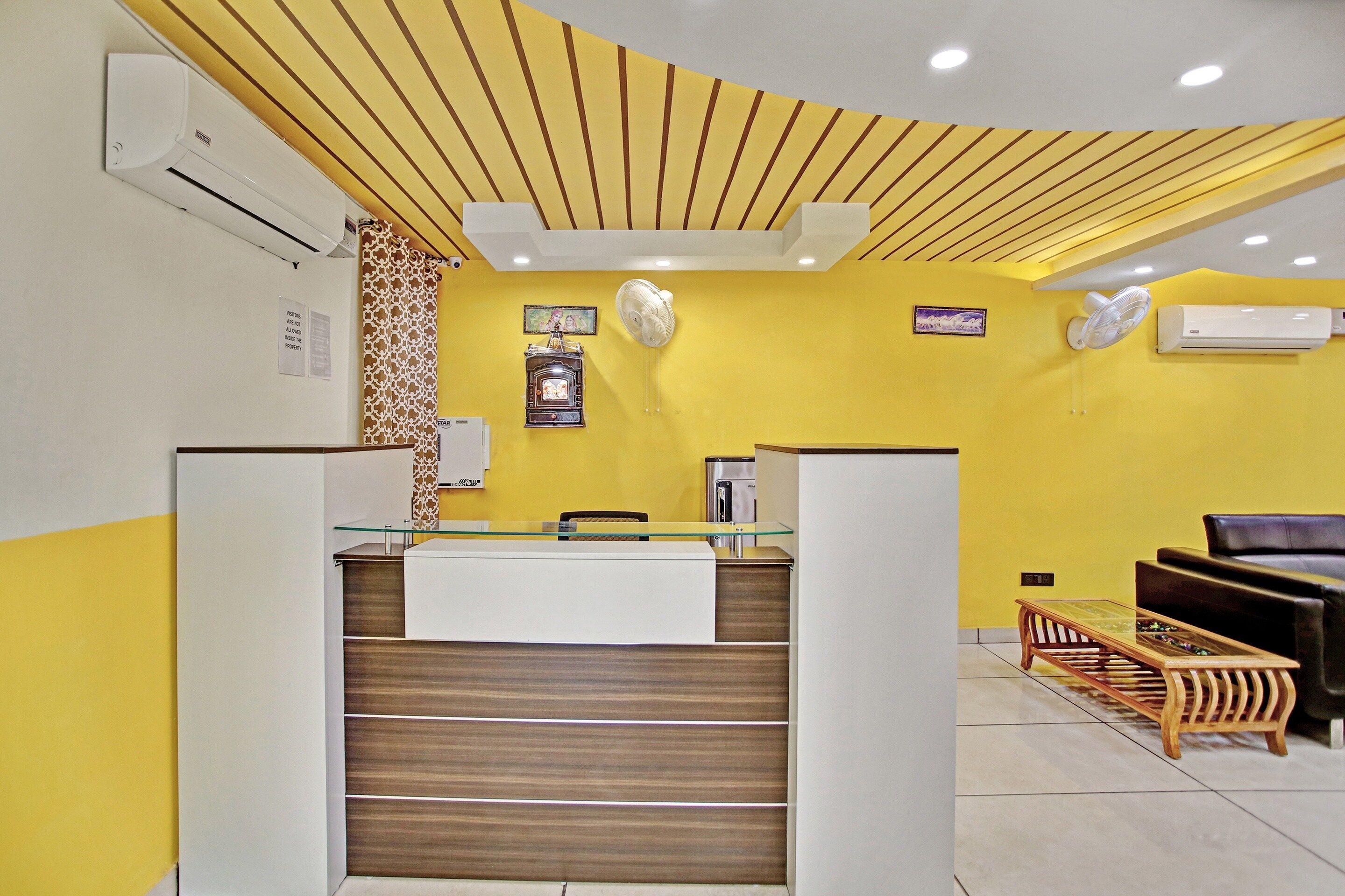 Un área de recepción con un mostrador de madera, un espacio de espera con un sofá y una mesita, y una unidad de aire acondicionado instalada en la pared.