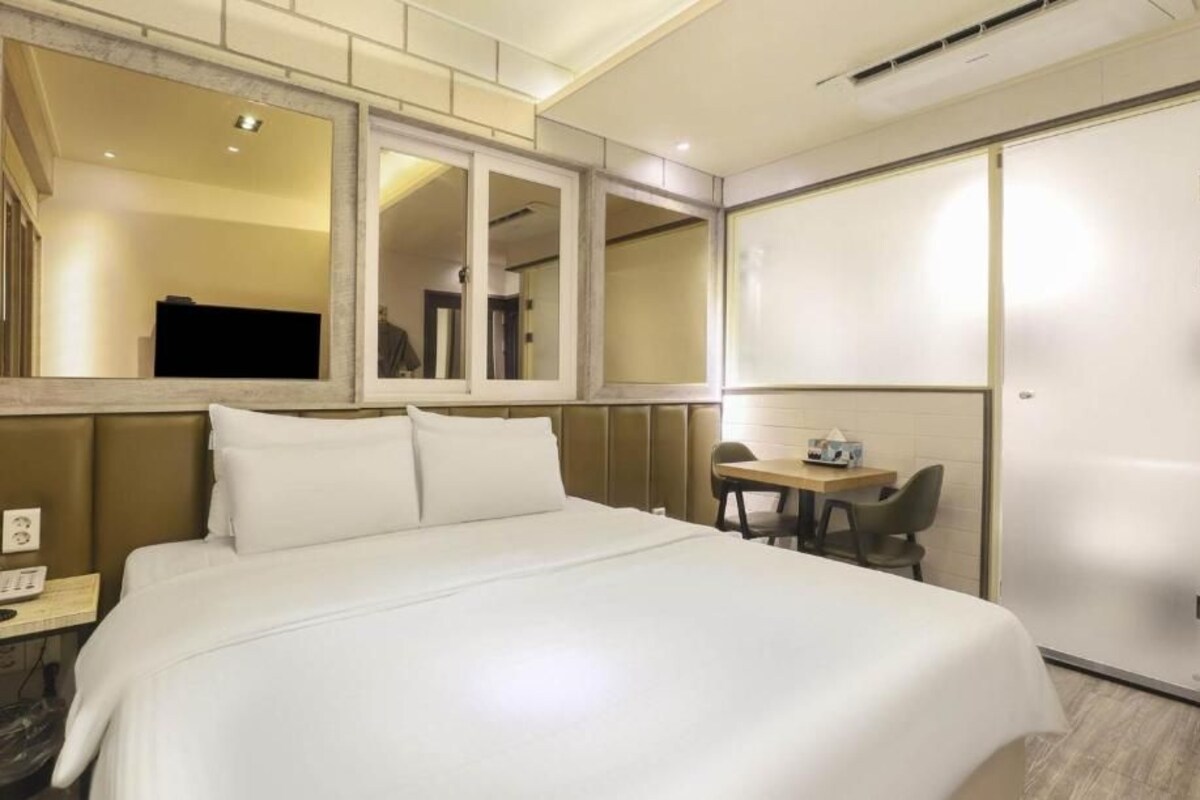 A hotel room with a large bed, a desk with a chair, a television, and a sliding door.