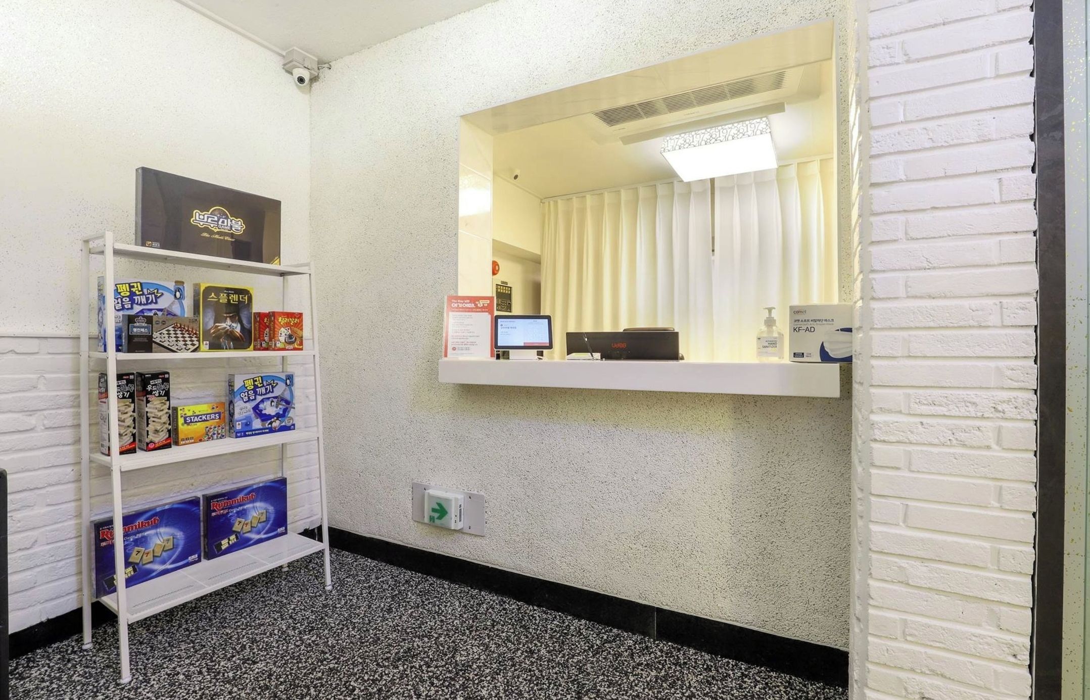 A reception area with a white brick wall, a reception desk with a computer and a telephone, and a shelf with board games.