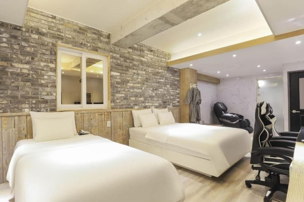 A hotel room with two beds, a wooden wall, a mirror, a chair, and a desk.
