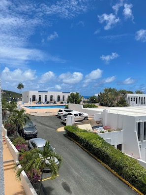 A resort with a pool, parked cars, and a clear blue sky.