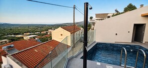 Ein Pool auf dem Dach mit Glasgeländer, freier Blick auf die umliegende Landschaft und ein rotes Ziegeldach.
