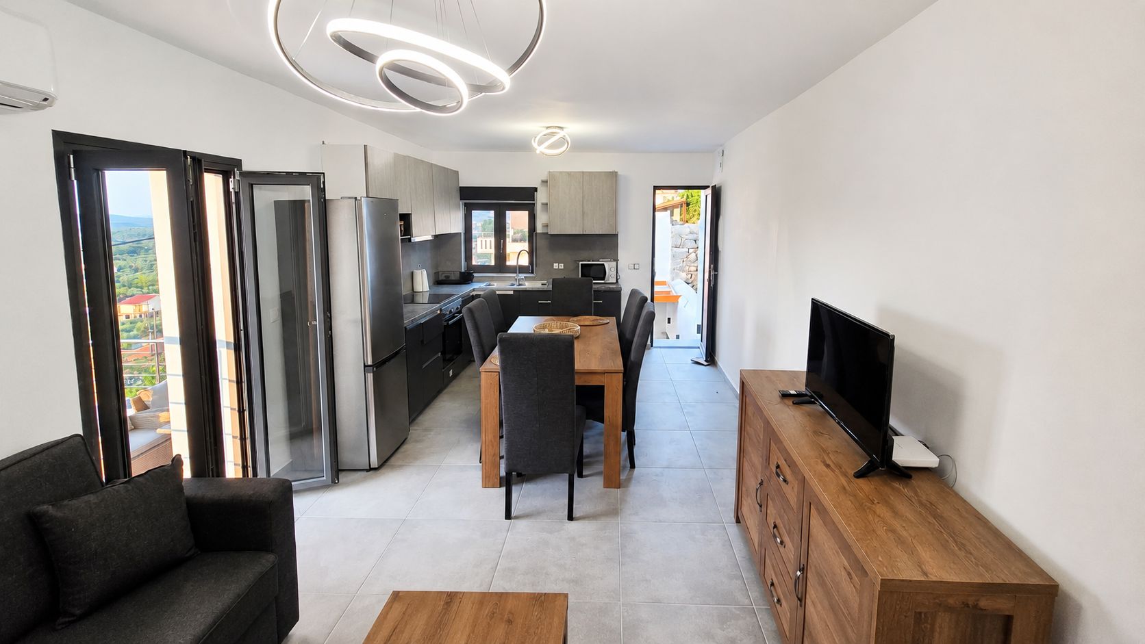 A modern kitchen with a dining area, a TV on a wooden cabinet, and a sofa.