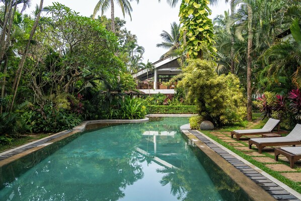 Une piscine aux eaux cristallines, entourée d’une végétation luxuriante, et un bâtiment doté d’un balcon.