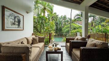 Una habitación con sofá, una mesa de comedor con comida y vistas a una piscina y follaje.