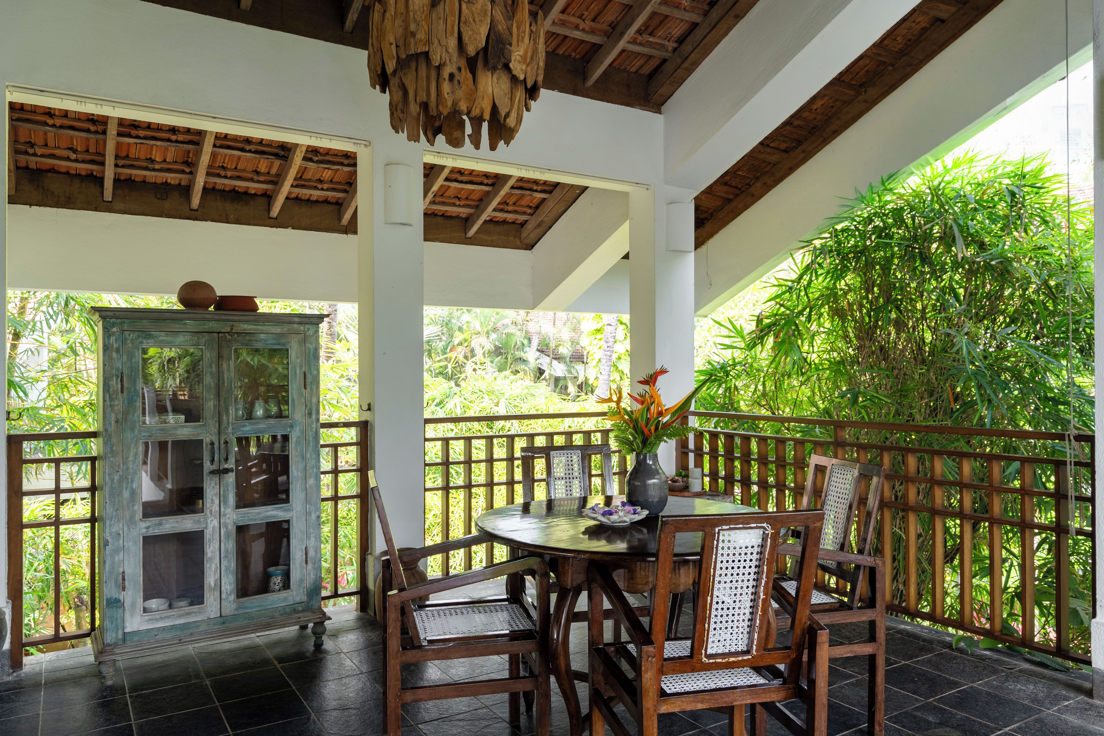 A covered outdoor seating area with a wooden table, chairs, and a cabinet.