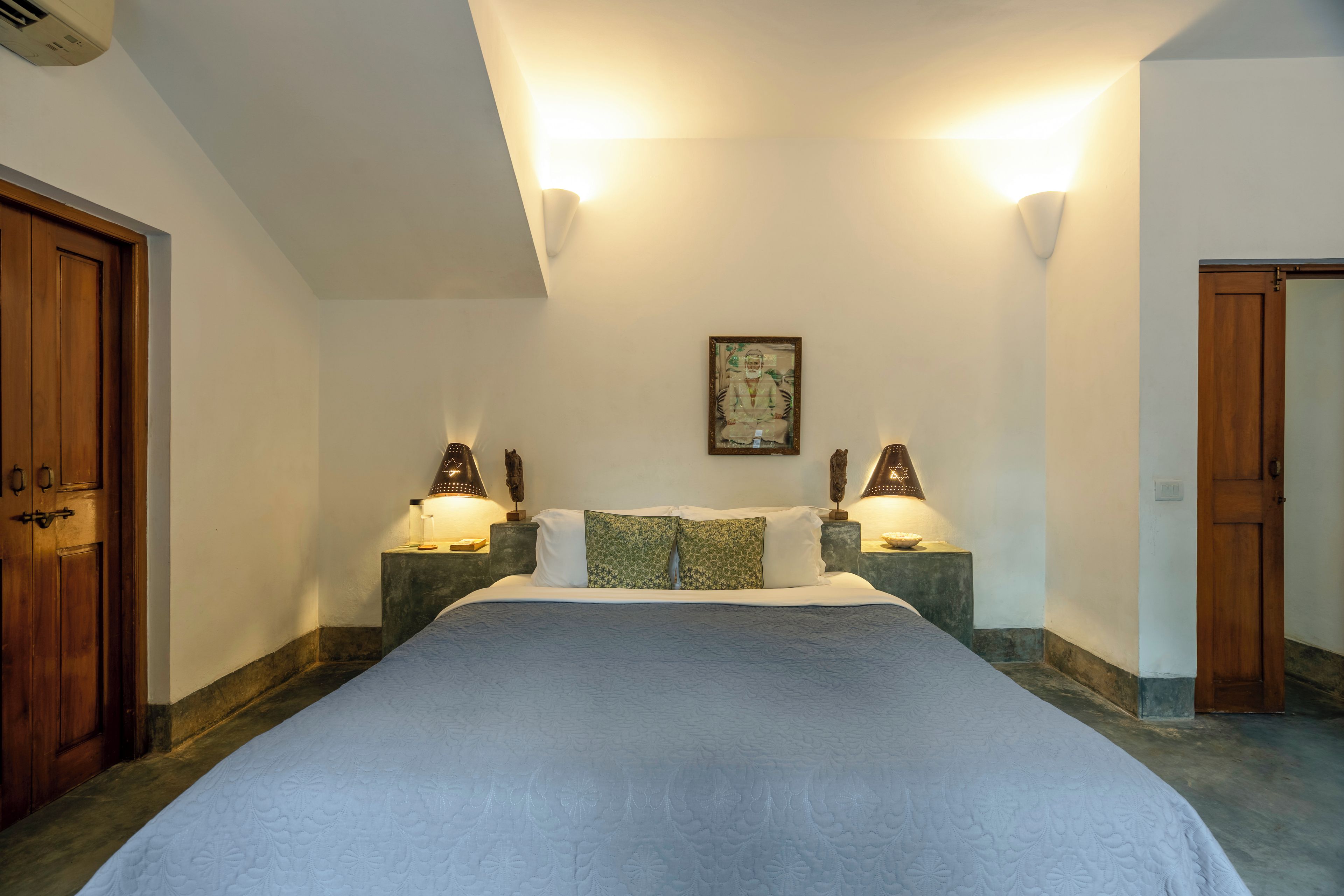 A bedroom with a large bed, two bedside lamps, a framed picture on the wall, and wooden doors.