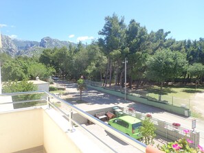Un balcon d’où l’on peut voir une voiture verte garée dans la rue, des arbres et, au loin, des montagnes.