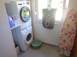 Un espace réduit dédié à la buanderie, comprenant un lave-linge, un étendoir et une poubelle de recyclage.