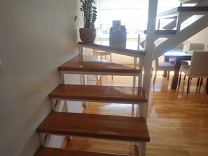 Un escalier avec des marches en bois et des rampes en métal mène à un espace repas comprenant des chaises et une table.