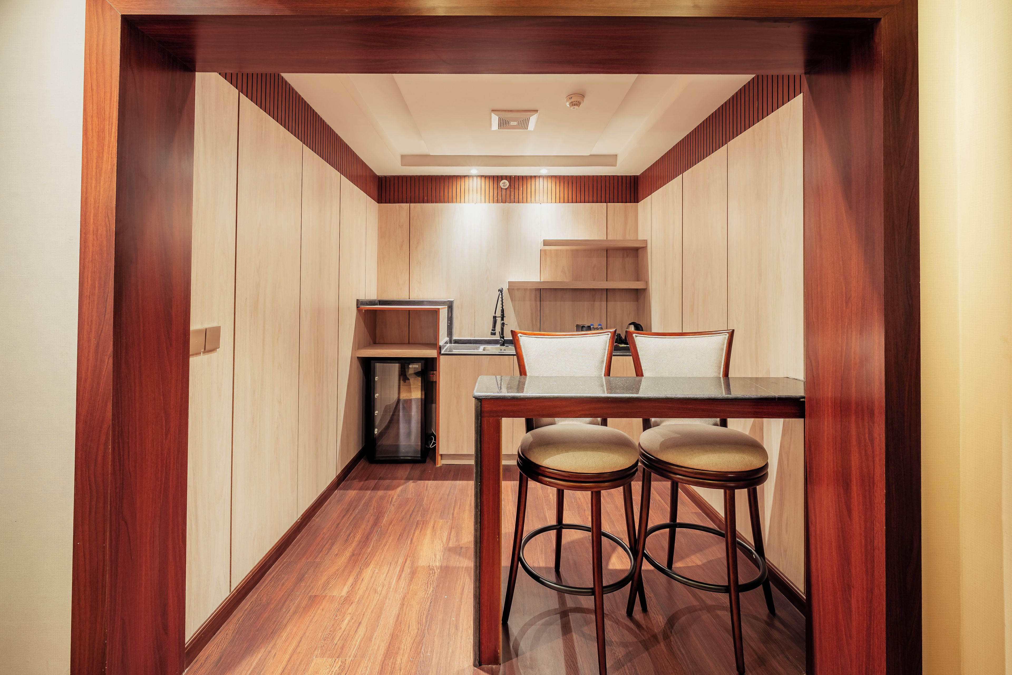 Cocina compacta con armarios de madera, refrigerador empotrado y una pequeña barra con taburetes.