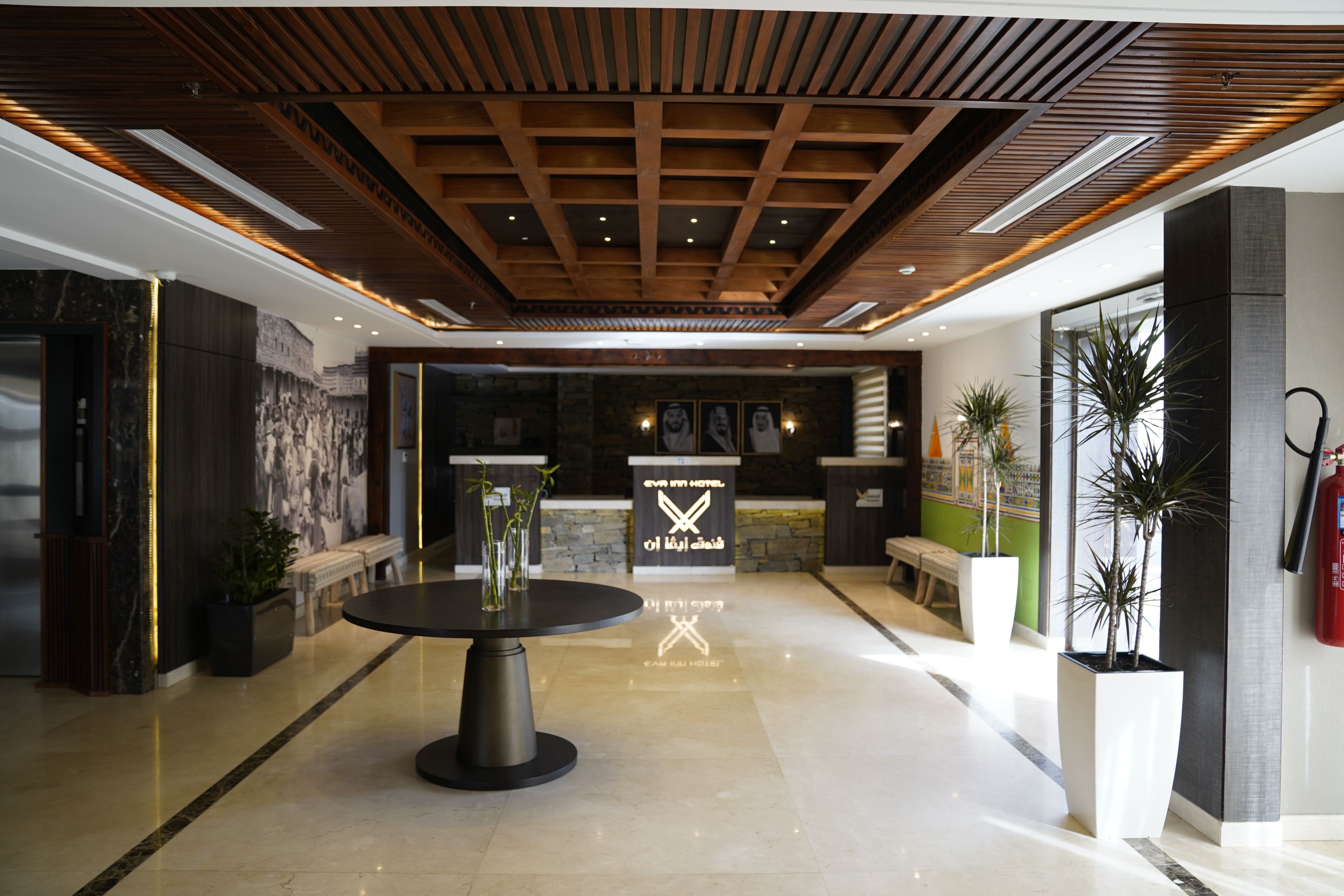 Een hotel lobby met een receptiebalie, een ronde tafel met vazen en een brandblusser.