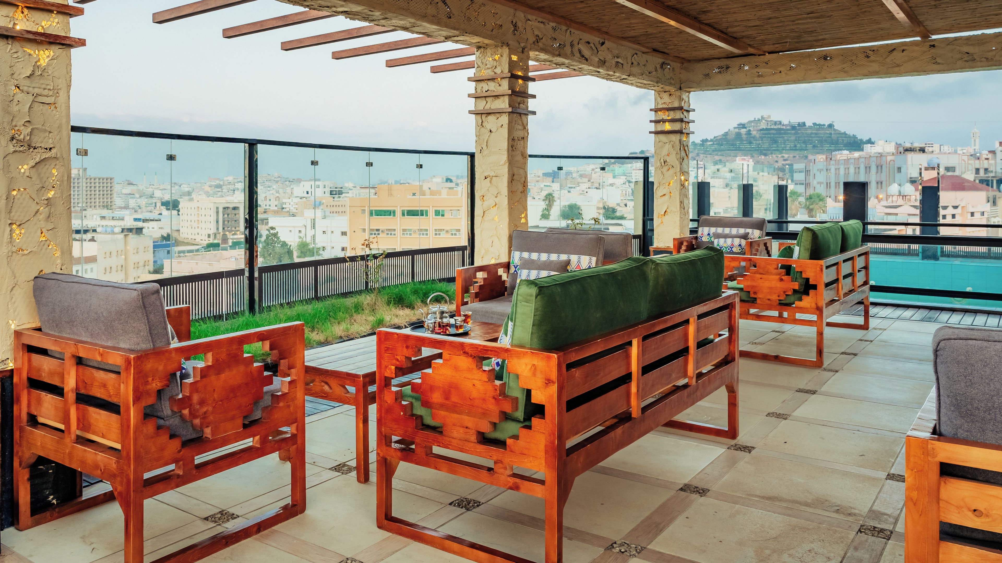 A rooftop terrace with wooden furniture, a view of the cityscape, and a pergola structure.