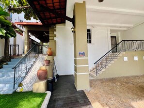 A staircase with a handrail, leading to a landing with a potted plant and a trash bin.