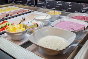 Un bufé con diversas opciones de comida, incluyendo queso, yogur y un postre rosado.