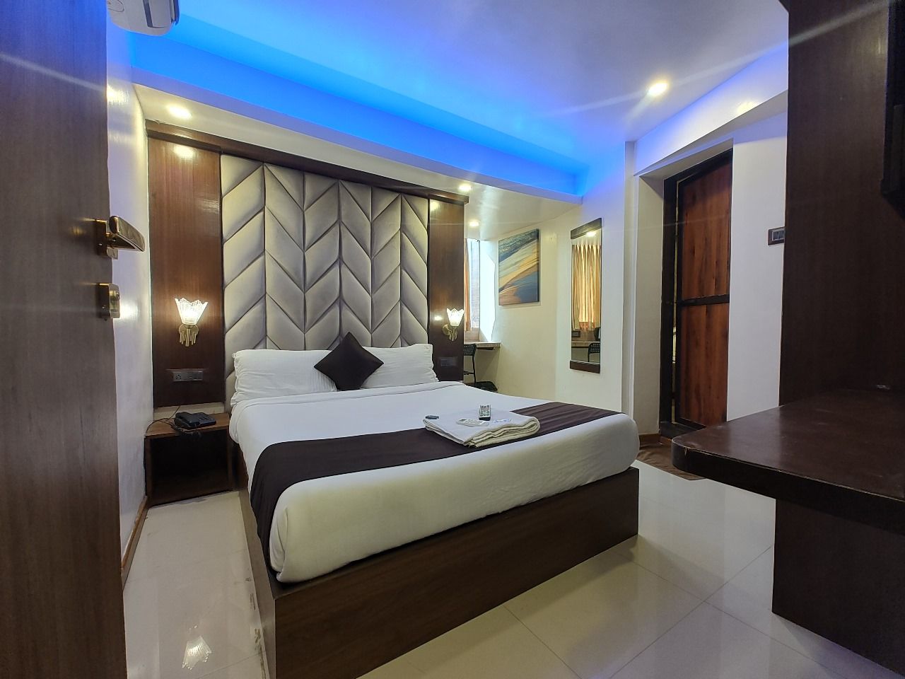 Una habitación de hotel moderna con una cama grande, una mesita de noche, una lámpara de pared y una luz de techo.