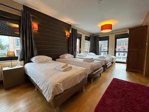 A hotel room with three beds, a red rug, and a view of the city. - Race & Rooms (Stavelot)