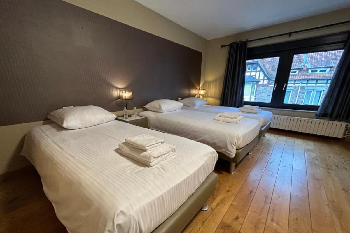 A hotel room with two beds, wooden flooring, and a view through a window.