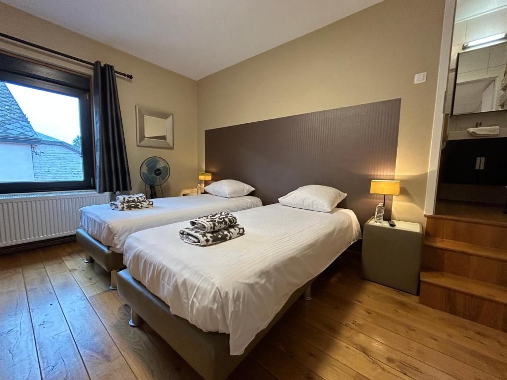 Habitación de hotel con dos camas, ventana con cortinas, un ventilador, una mesita de noche con lámpara y una escalera.