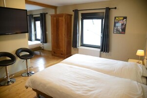 Habitación de hotel con dos camas, un armario de madera, un televisor y una ventana con cortinas.
