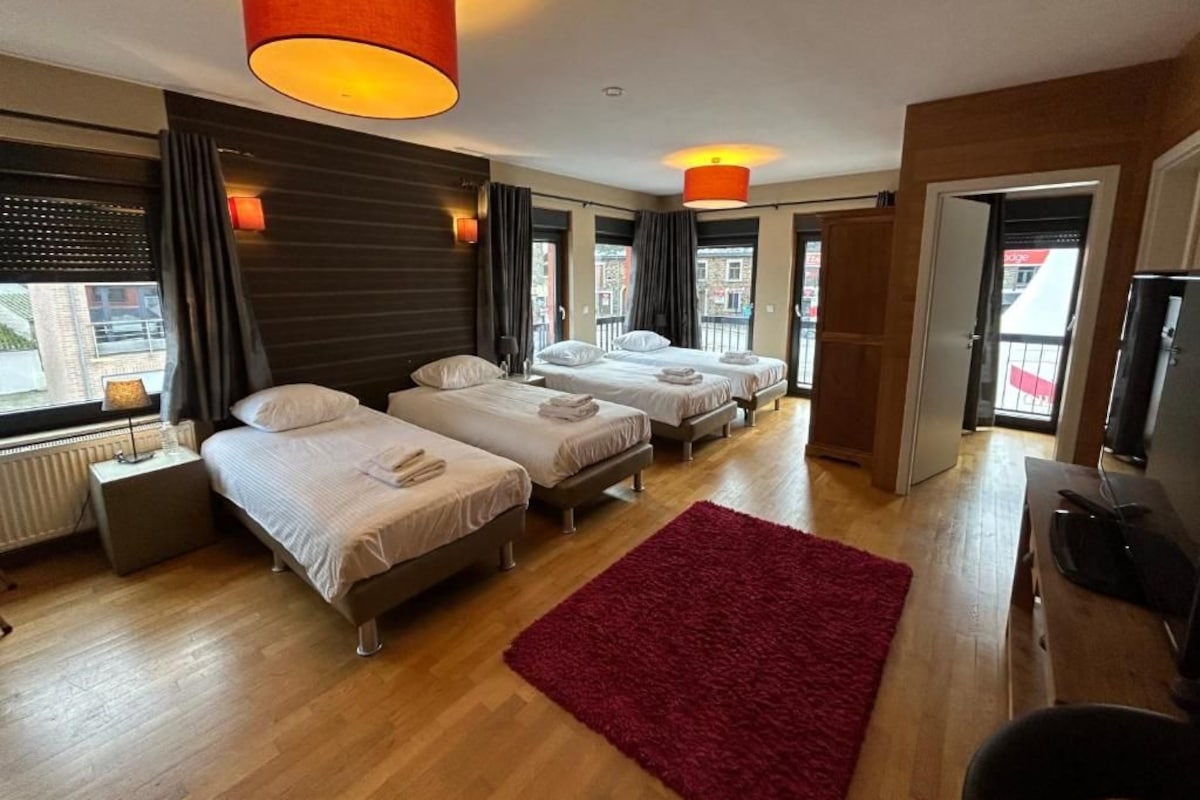 A hotel room with three beds, a red rug, and a wooden floor.
