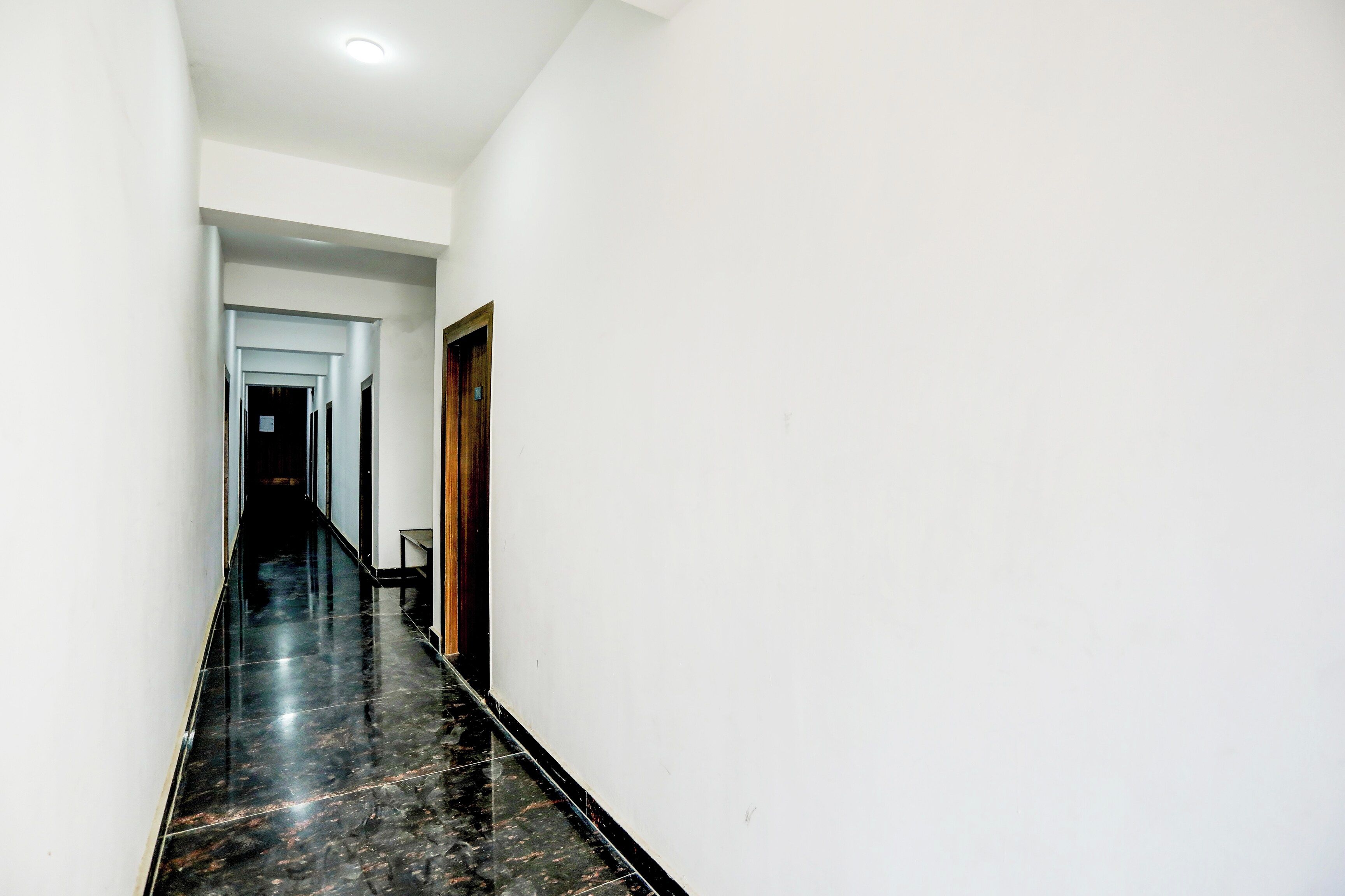 A corridor with a shiny black floor, white walls, and a wooden door.