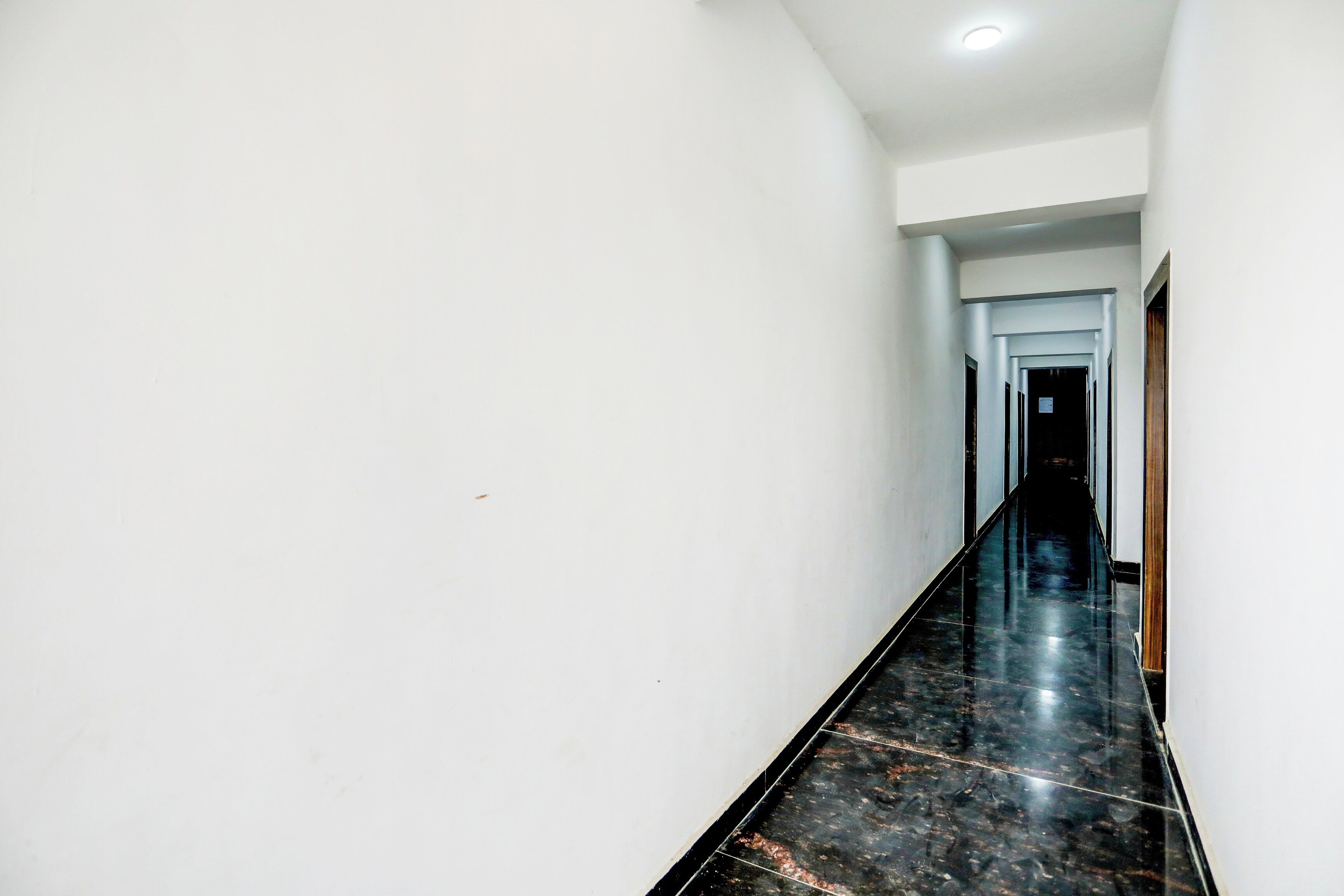 A long, narrow hallway with white walls and a black marble floor.