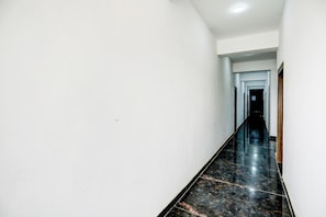 Um corredor comprido e estreito, com paredes brancas e chão de mármore preto.