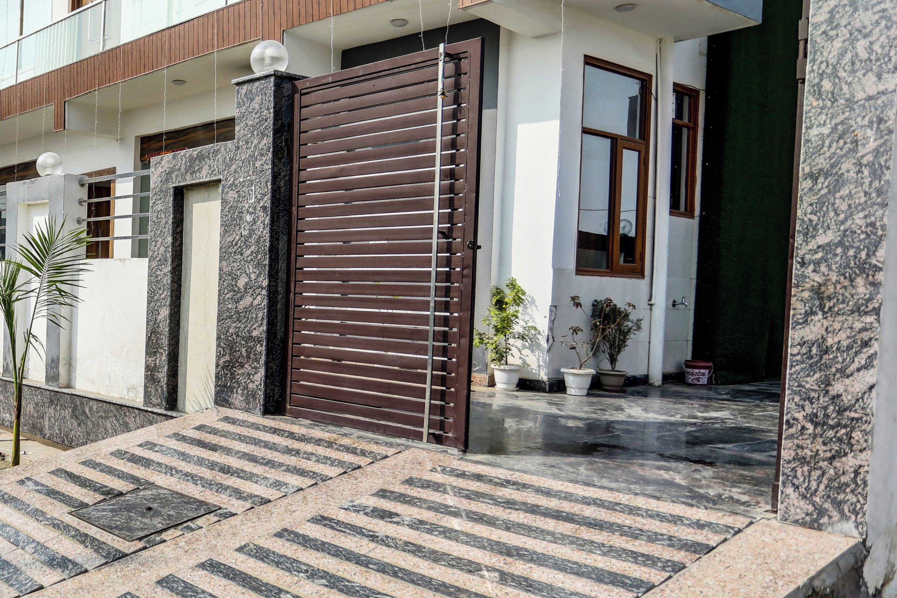 A modern house entrance with a large metal gate, potted plants, and a marble floor.