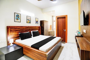 A hotel room with a wooden headboard, a bed with black and white bedding, a bedside table with a lamp, a wardrobe, a bathroom with a shower, and a TV mounted on the wall. - Hotel O Galaxy inn (Noida)